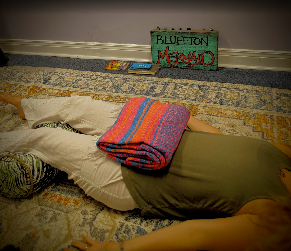 Client resting on the floor in a supported restorative pose with bolsters and blankets