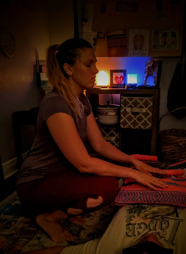 Laurel seated in a candlelit treatment room with hands resting on a client's bolster